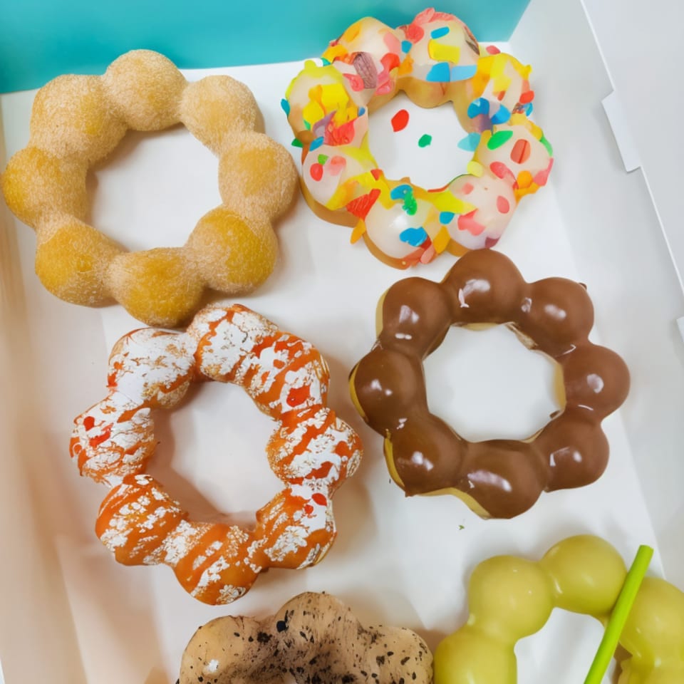 A box of colorful Love Me Mochi donuts with various glazes and toppings.