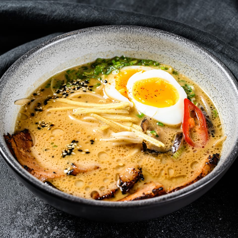 A bowl of ramen with a soft-boiled egg, pork, green onions, and red chili in a rich broth.